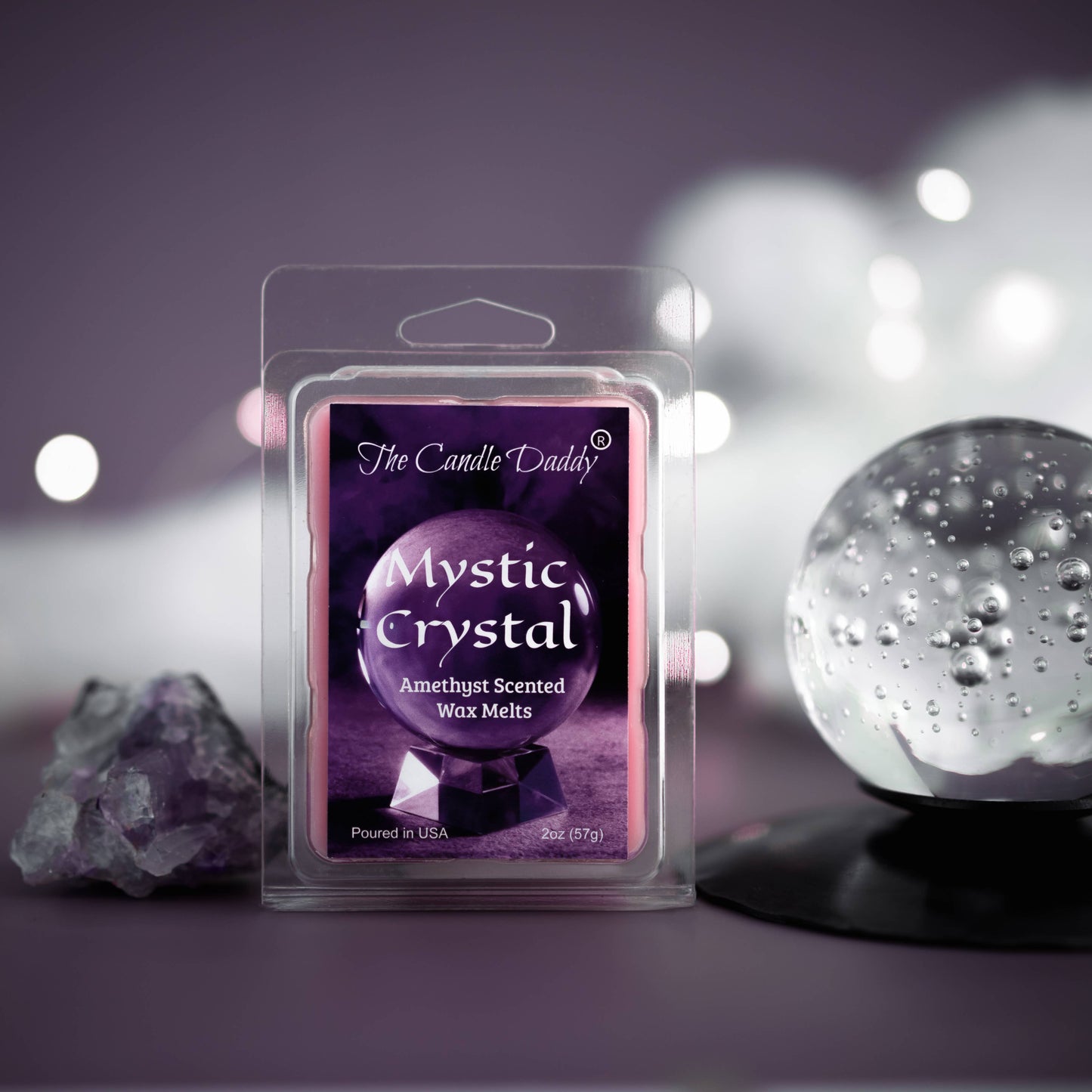 A packaged 'Mystic Crystal' amethyst scented wax melt by The Candle Daddy, with a purple label and a clear plastic cover, displayed next to a crystal ball and decorative lights.